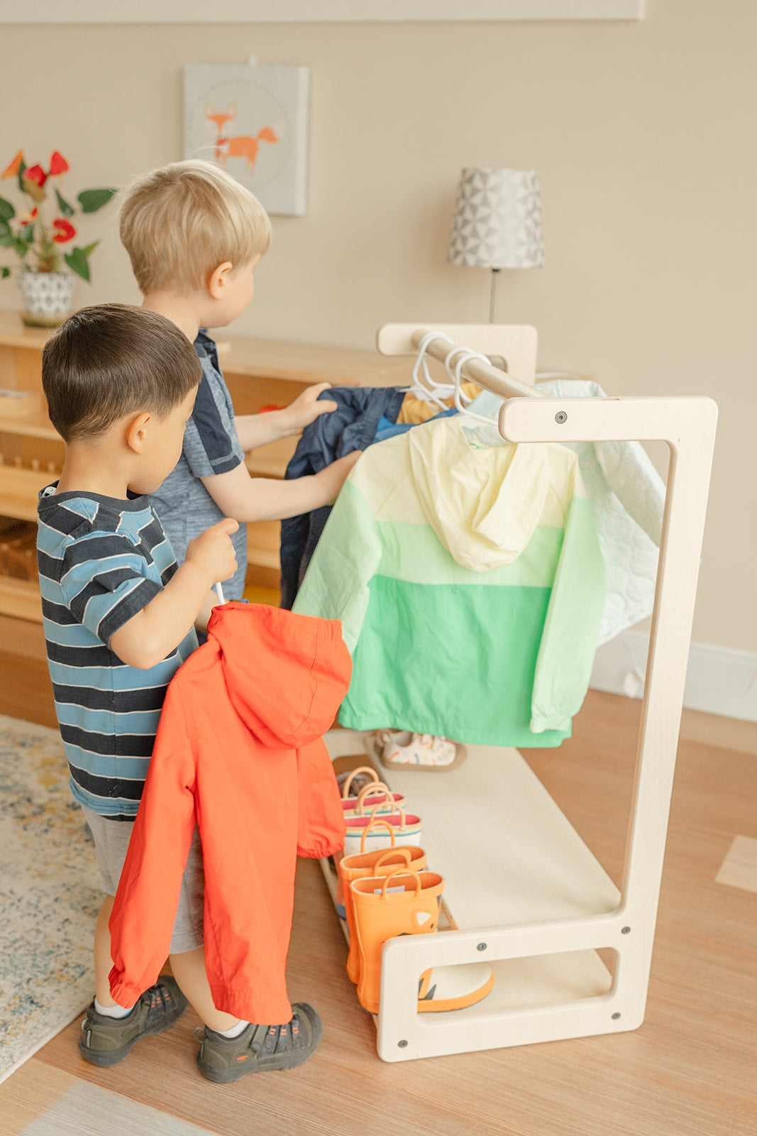 Two preschool aged boys in a Montessori classroom picking their jackets from the child size clothing rack