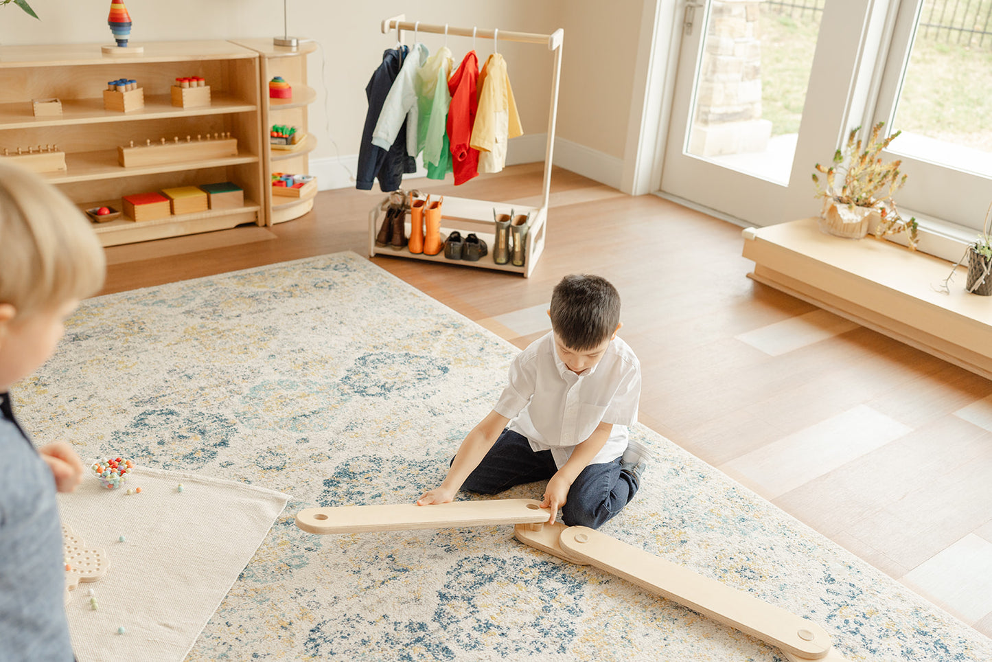 Primary Montessori aged boy putting together a long wooden balance beam on the ground to make an obstacle course