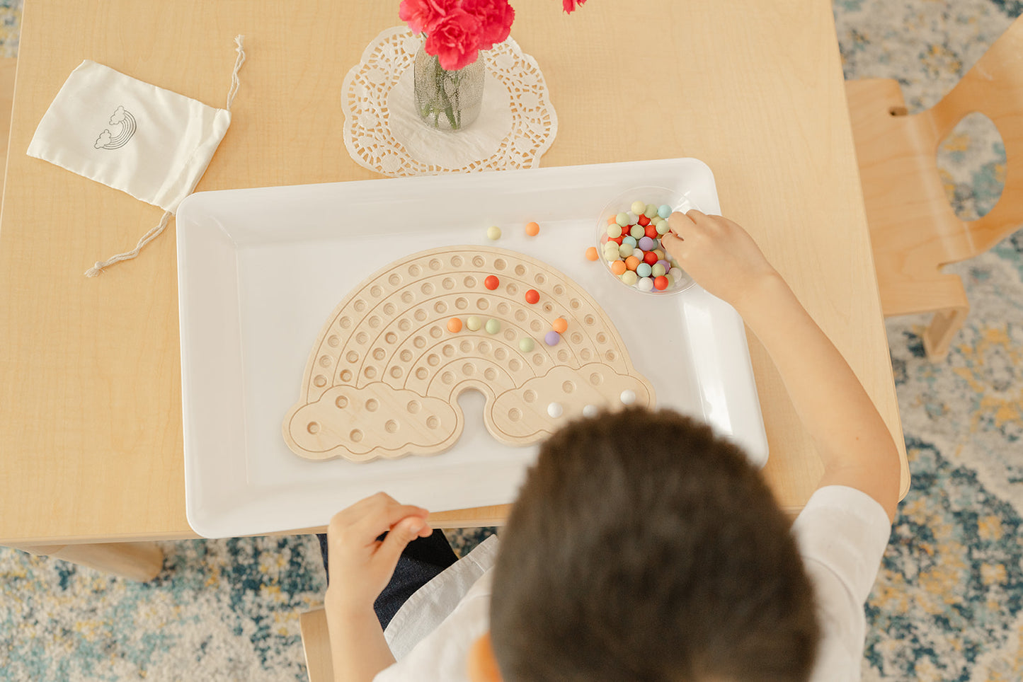 Five year old boy in a Montessori Primary classroom placing colorful wooden balls on rainbow board. A bowl of colorful wooden balls are placed next to rainbow board to pick from and create endless designs on rainbow board. Great activity for patterns, counting, and creativity.