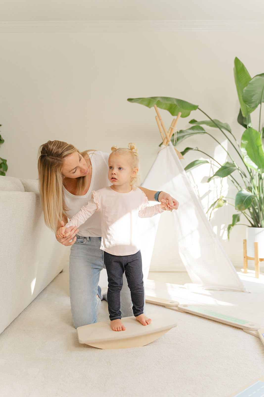 A mother helping her young kid to use a balance board and improve her balance