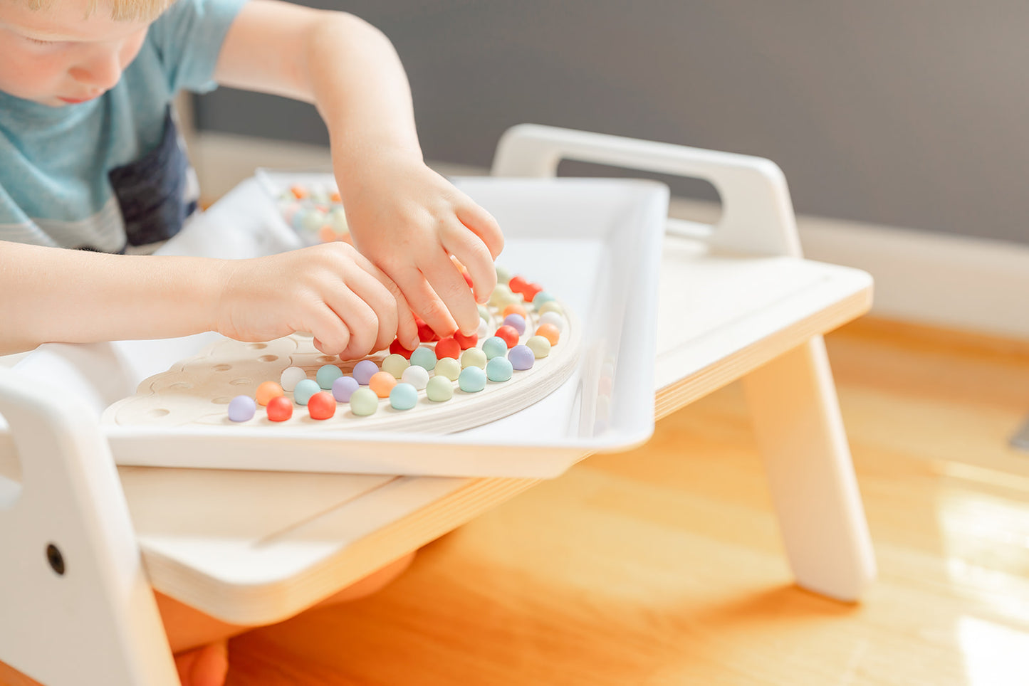 Five year old boy focused and honing his fine motor development with the Montessori Rainbow Activity Board. A bowl of colorful wooden balls are placed next to rainbow board to pick from and create endless designs on rainbow board.