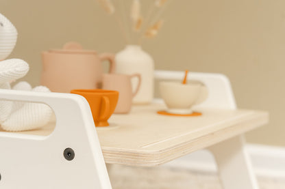 a beautiful set up on a small wooden white framed table, meant for children activities such as eating, playing, or working.