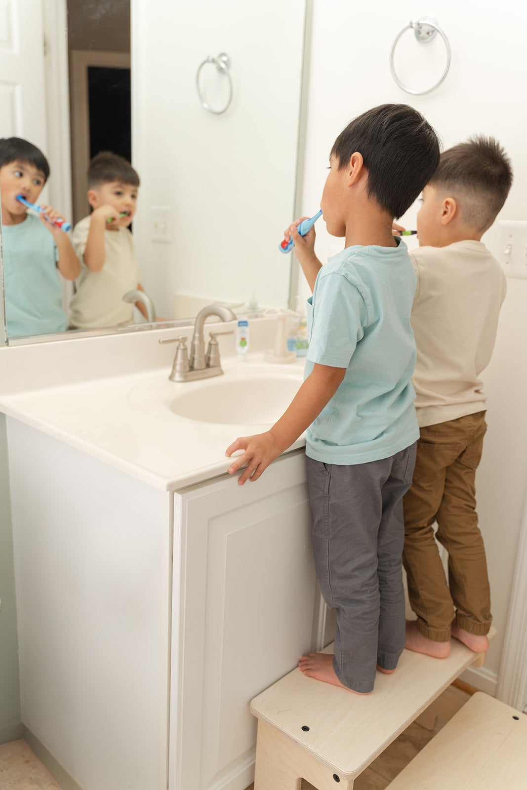 Two toddlers comfortably standing together on extra-wide wooden kitchen helper stool without crowding, double kids step stool with generous platform reducing sibling rivalry during cooking and bathroom routines, Montessori learning stool wider than standard single-child kitchen towers accommodating siblings simultaneously, wooden helper stool perfect for families with multiple young children sharing kitchen and bathroom spaces.