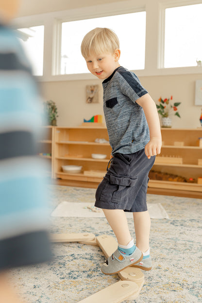 Little boy smiling while walking and balancing on a modular wooden balance beam in a classroom setting