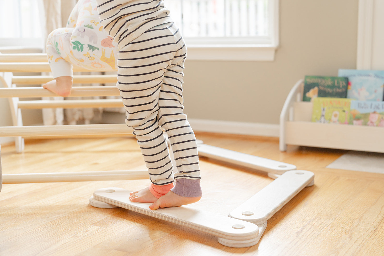 Little feet standing on a wooden modular balance beam in a playroom, the beam is used to work on Pediatric occupational and physical therapy 