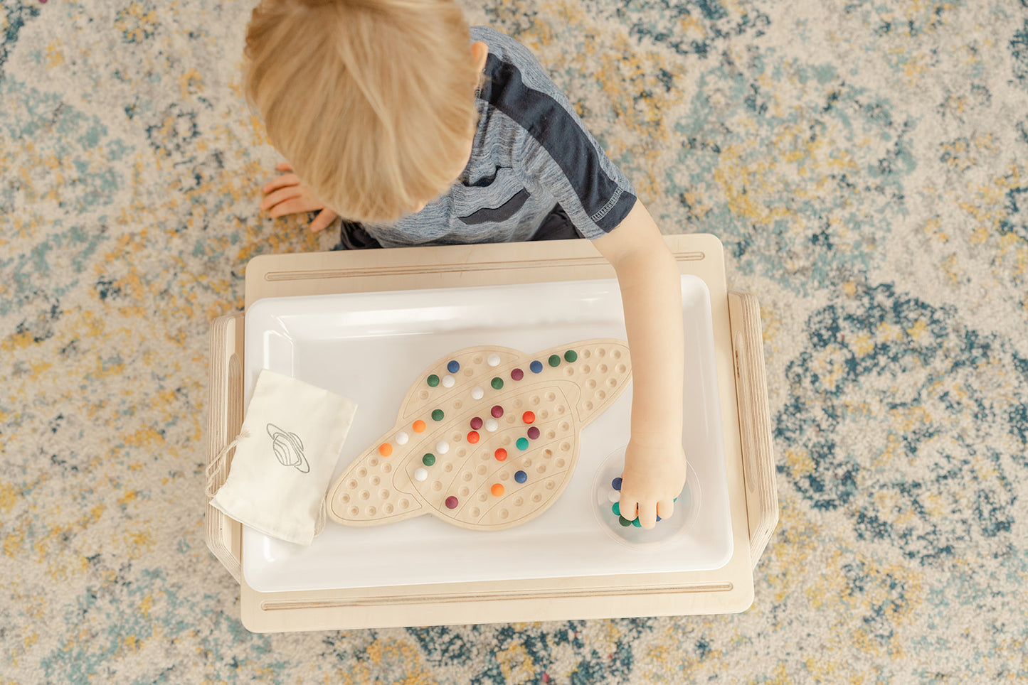 young boy working on a space themed wooden activity placing colorful wooden balls in a design on a Saturn activity board