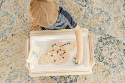 young boy working on a space themed wooden activity placing colorful wooden balls in a design on a Saturn activity board