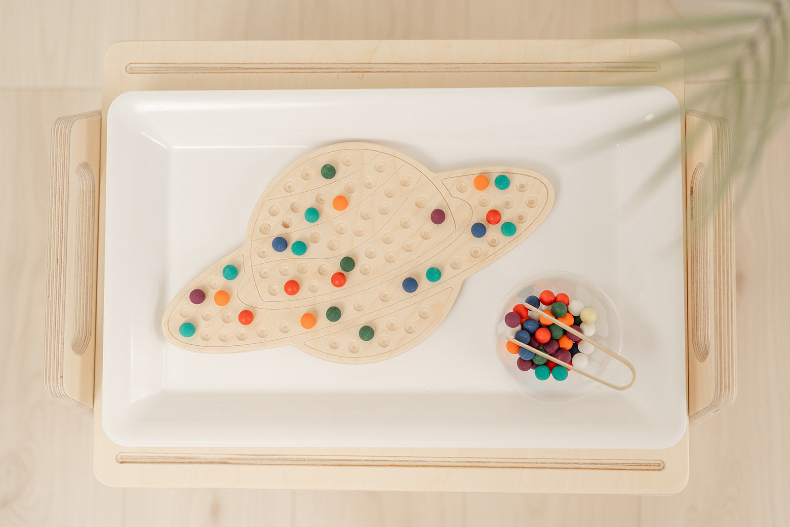 Product photo of Montessori wooden saturn board and bowl of colorful wooden balls with bamboo tong. The multi-colored balls add a tactile sensory dimension and appeals to kids with ADHD. The bamboo tong adds a fine motor challenge for older students.