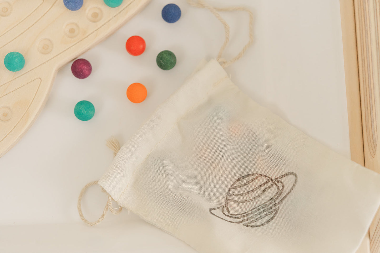 Montessori materials with wooden Saturn board and colorful wooden balls. The canvas bag is placed next to the wooden space activity and holds the 98 colorful wooden balls and bamboo tong provided with the educational preschool toy.