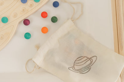 Montessori materials with wooden Saturn board and colorful wooden balls. The canvas bag is placed next to the wooden space activity and holds the 98 colorful wooden balls and bamboo tong provided with the educational preschool toy.