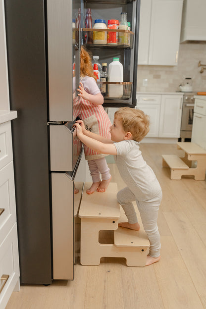 Blueberry and Third wide wooden step stool with two toddlers in mini chef aprons helping with dinner, best kitchen helper stool for little chefs ages 2 and up