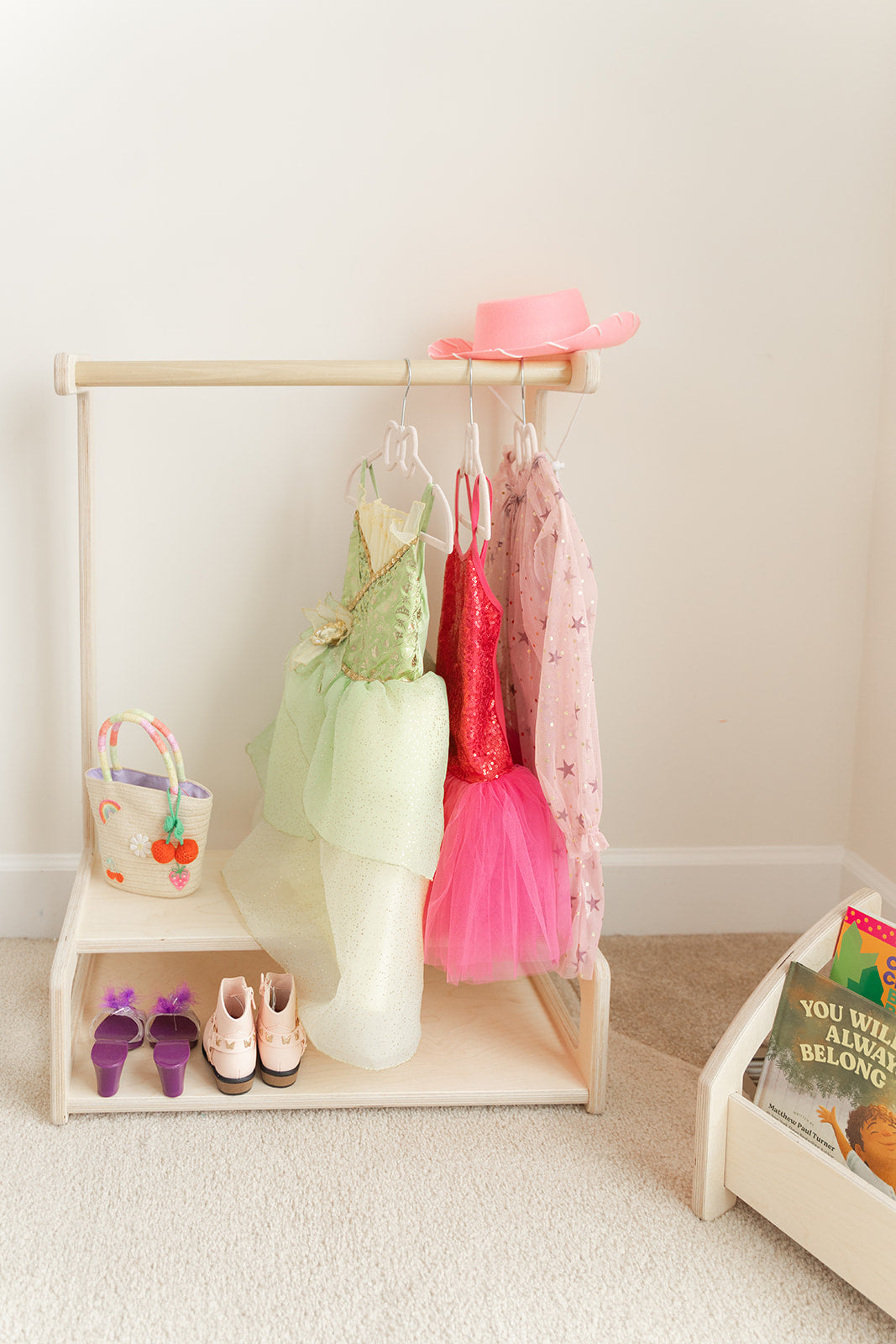 Blueberry and Third kids clothing rack with lower storage shelves and wooden dowel rod, toddler clothes displayed at child height for independent dressing
