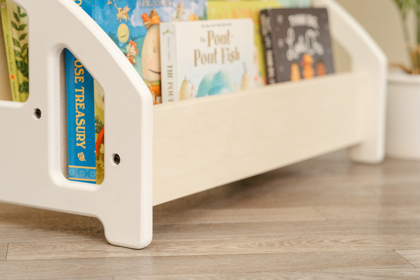 Angled profile of a low to ground childrens bookshelf with white frames and natural wood front.