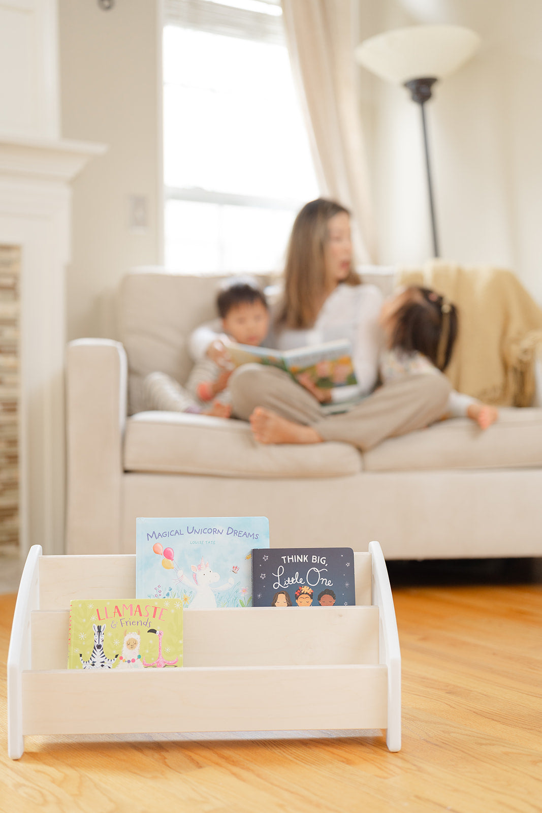 A bookshelf placed in front of a couch with a mother reading to her children