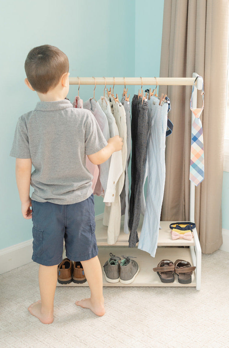 A boy choosing what to wear from a kid-size clothing rack