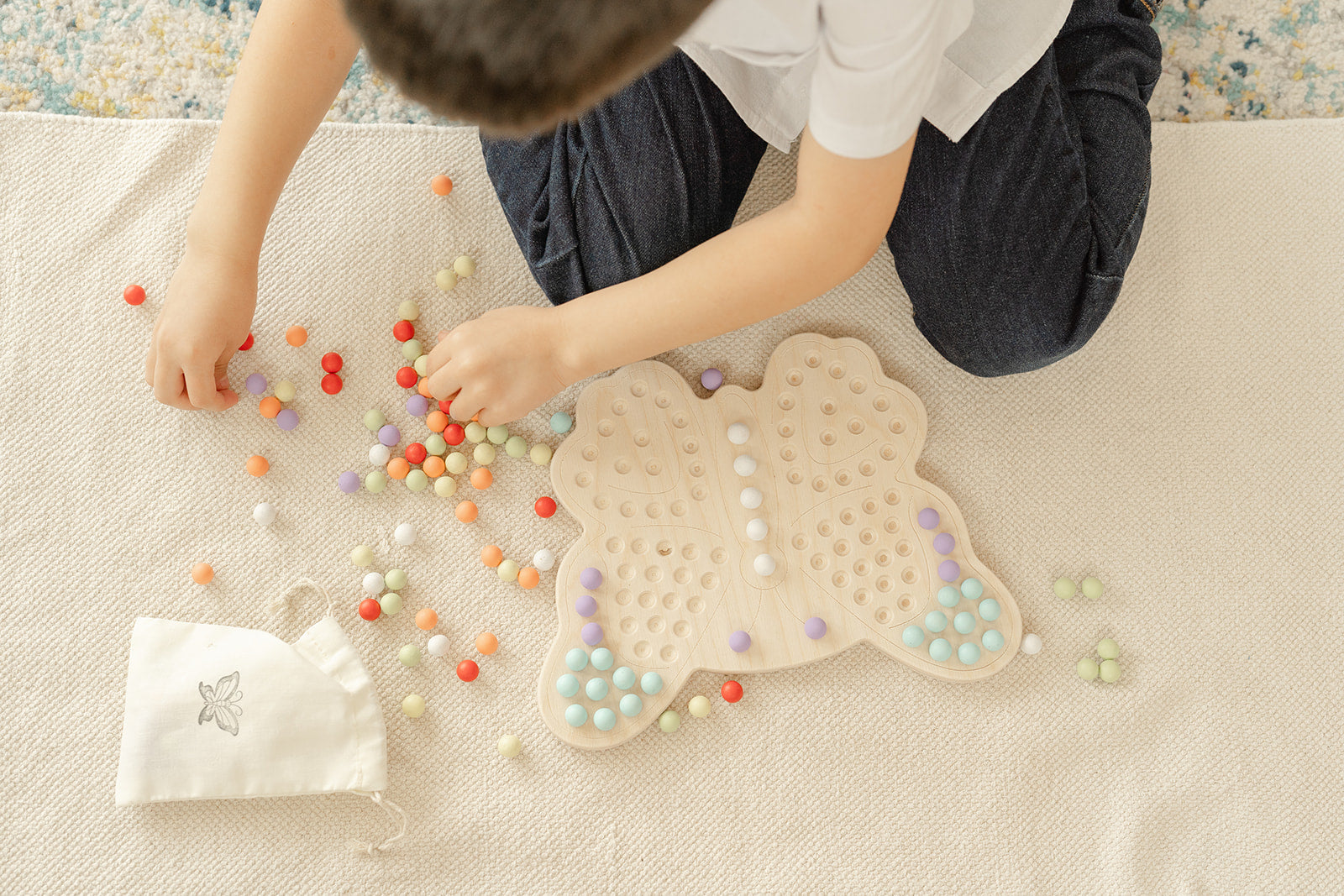 Preschooler sorting rainbow-colored wooden balls by color on butterfly Montessori activity board learning color recognition and categorization skills. Educational peg board toy for ages 3-6 promoting early math concepts through hands-on sorting matching and organizing activities. Wooden sensory toy encouraging logical thinking decision-making and cognitive development through open-ended color sorting games and creative play scenarios in screen-free learning environment.