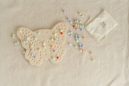 Wooden butterfly activity board displayed in modern Montessori playroom with neutral decor demonstrating how educational toys integrate into home environment. Screen-free sensory peg board for ages 3-6 providing quiet focused activity for preschoolers. USA-made wooden toy complementing minimalist playroom aesthetic while offering valuable hands-on learning experience developing fine motor skills creativity and independent play habits through open-ended Montessori-inspired design.