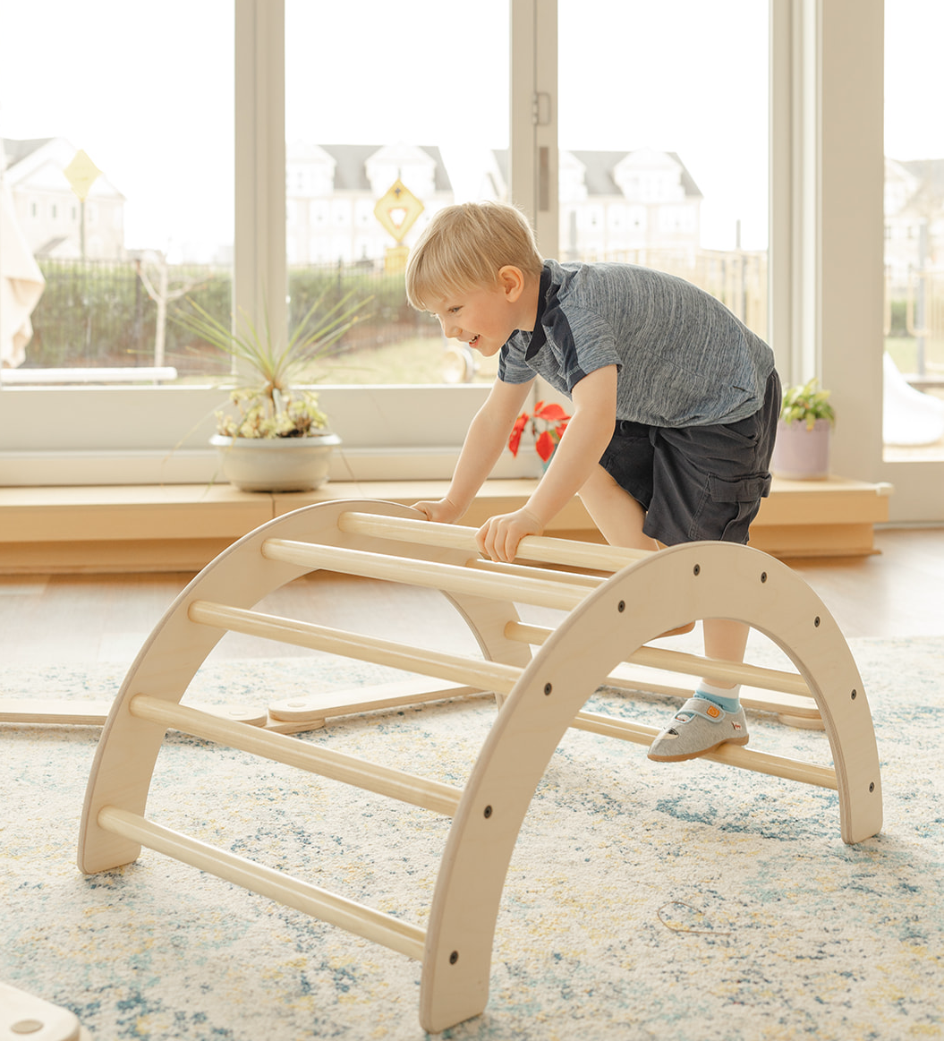 young boy climbing over natural finish toddler climbing arch in a montessori classroom