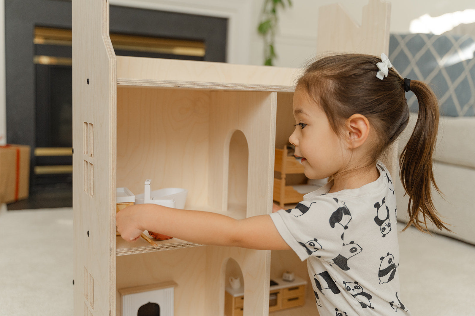A young girl playing with a wooden dollhouse and miniature figurines 