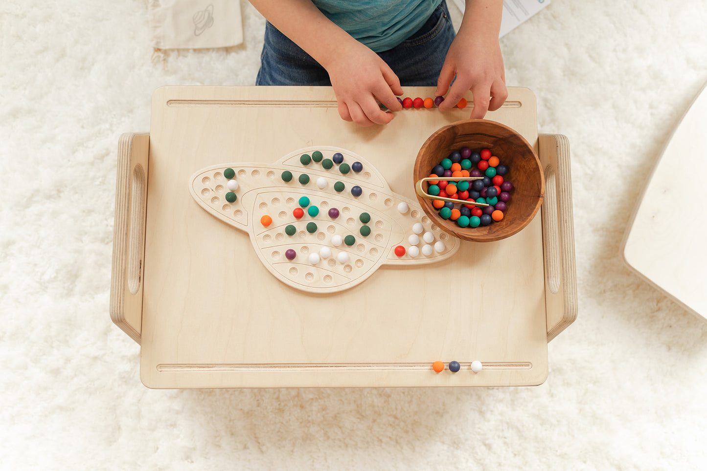 Child creating imaginative design with colorful wooden pegs on Saturn activity board showcasing unlimited pattern-making possibilities for ages 3-8. Educational space-themed peg board encouraging artistic creativity problem-solving and critical thinking through open-ended STEM play. Montessori learning toy with no right or wrong way to play fostering confidence experimentation and creative exploration through hands-on tactile manipulation in screen-free educational play environment perfect for elementary st