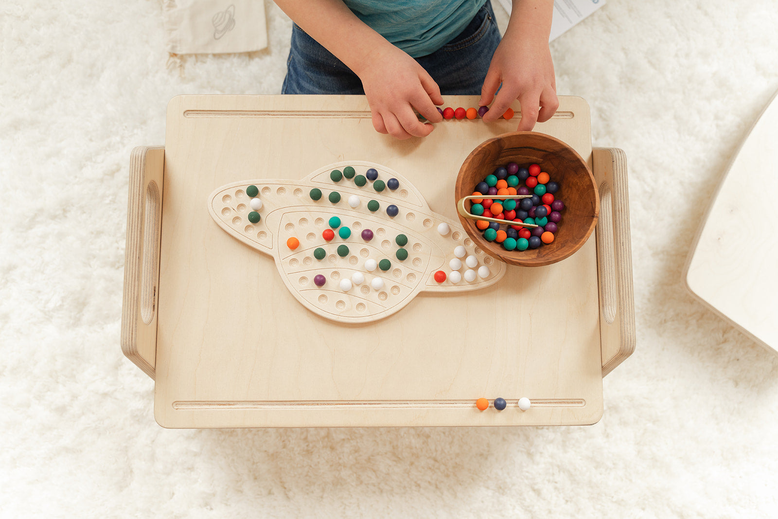 Child creating imaginative design with colorful wooden pegs on Saturn activity board showcasing unlimited pattern-making possibilities for ages 3-8. Educational space-themed peg board encouraging artistic creativity problem-solving and critical thinking through open-ended STEM play. Montessori learning toy with no right or wrong way to play fostering confidence experimentation and creative exploration through hands-on tactile manipulation in screen-free educational play environment perfect for elementary st