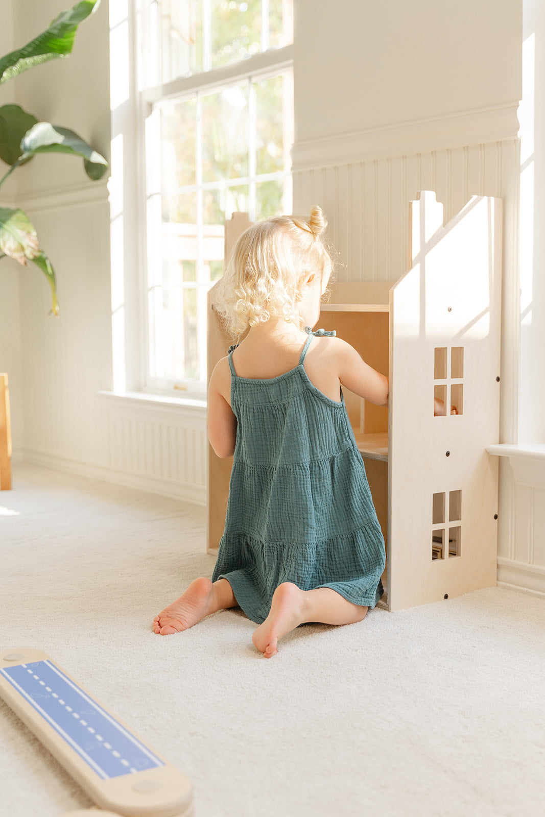 A girl playing with a dollhouse in a sunny room