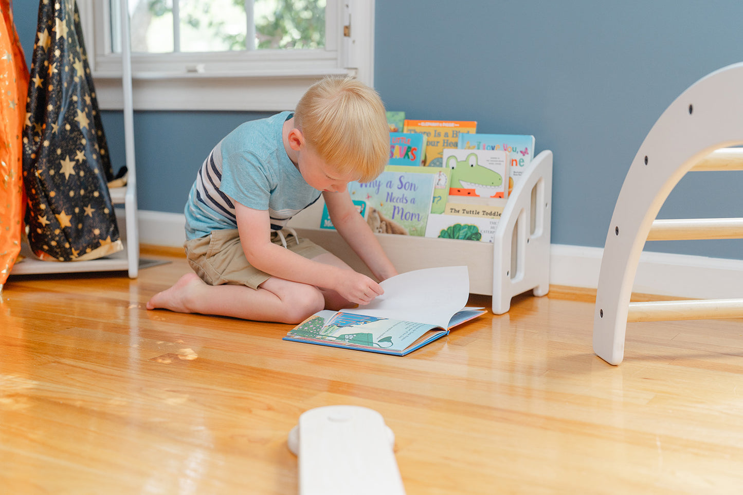 A child reading a book that was taken from the floor bookshelf in a bedroom