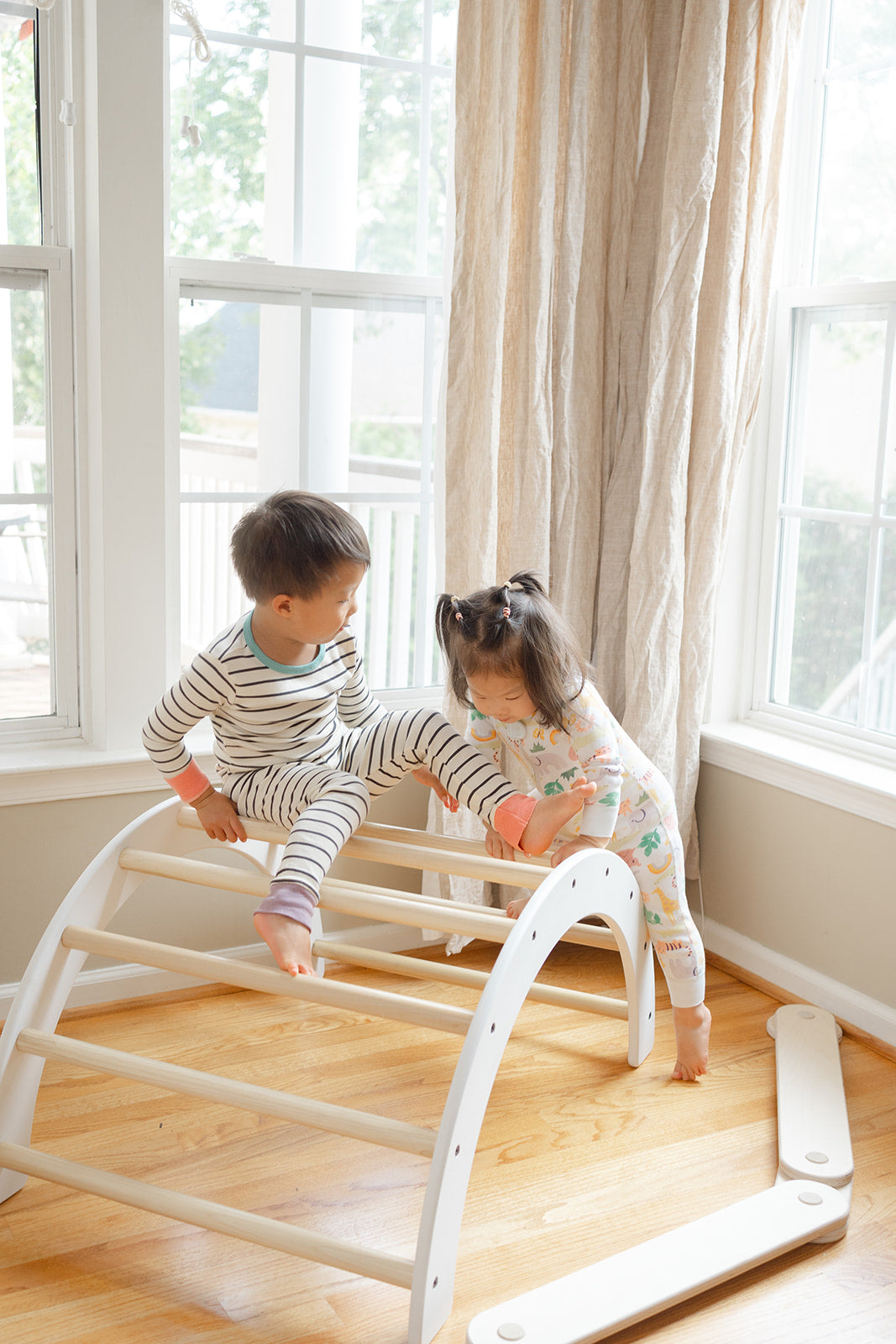 Two children playing on a wooden montessori climbing arch