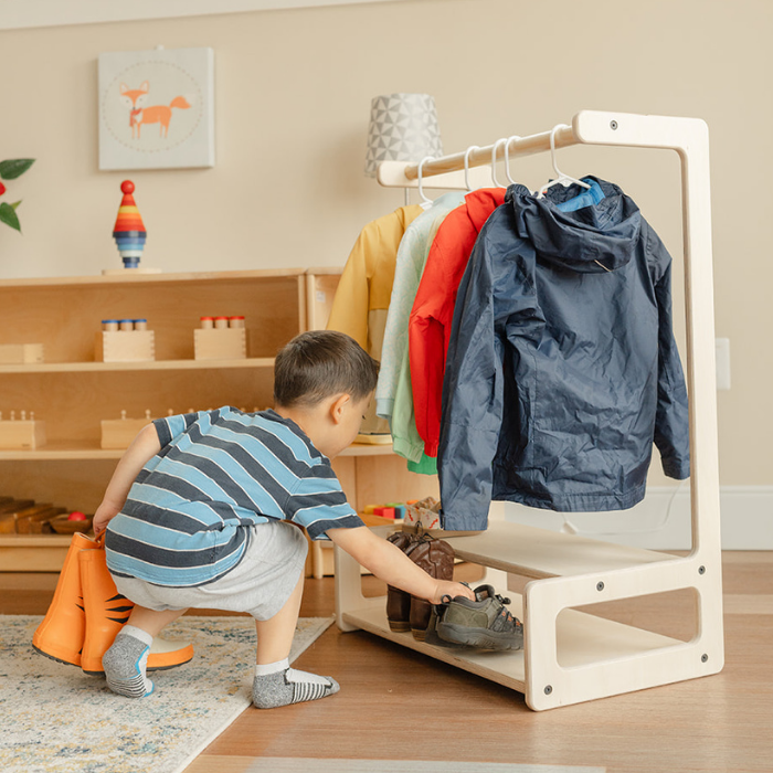 Preschool aged boy in a Montessori classroom picking his sneakers from the shelf on the nautral wood child size clothing rack 