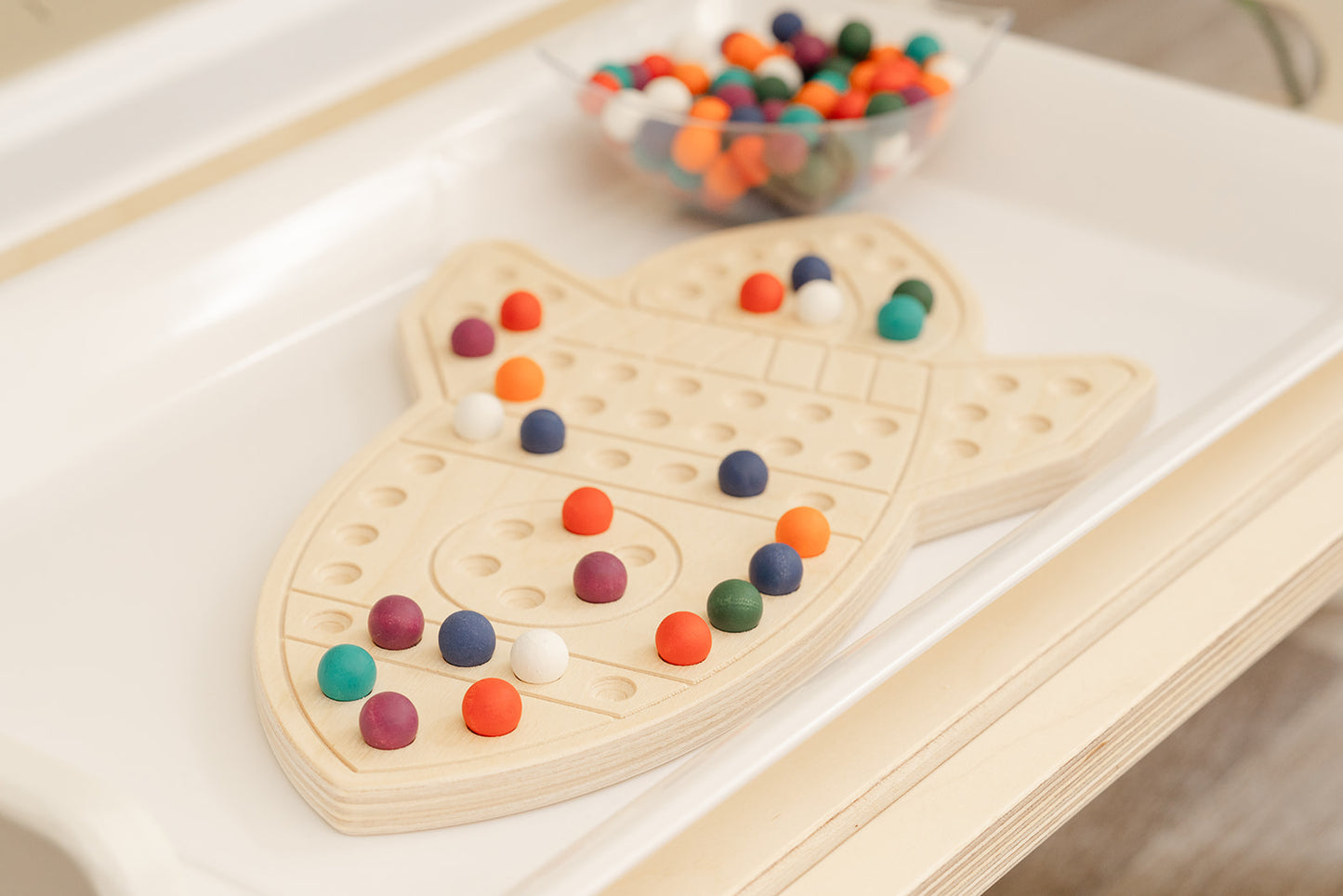 Wooden space activity board displayed in modern educational playroom with neutral decor demonstrating how STEM toys integrate into home environment. Screen-free sensory peg board for ages 3-6 providing quiet focused learning activity for preschoolers. USA-made wooden educational toy complementing minimalist playroom aesthetic while offering valuable hands-on STEM learning experience developing fine motor skills creativity and independent play habits through Montessori-inspired design.