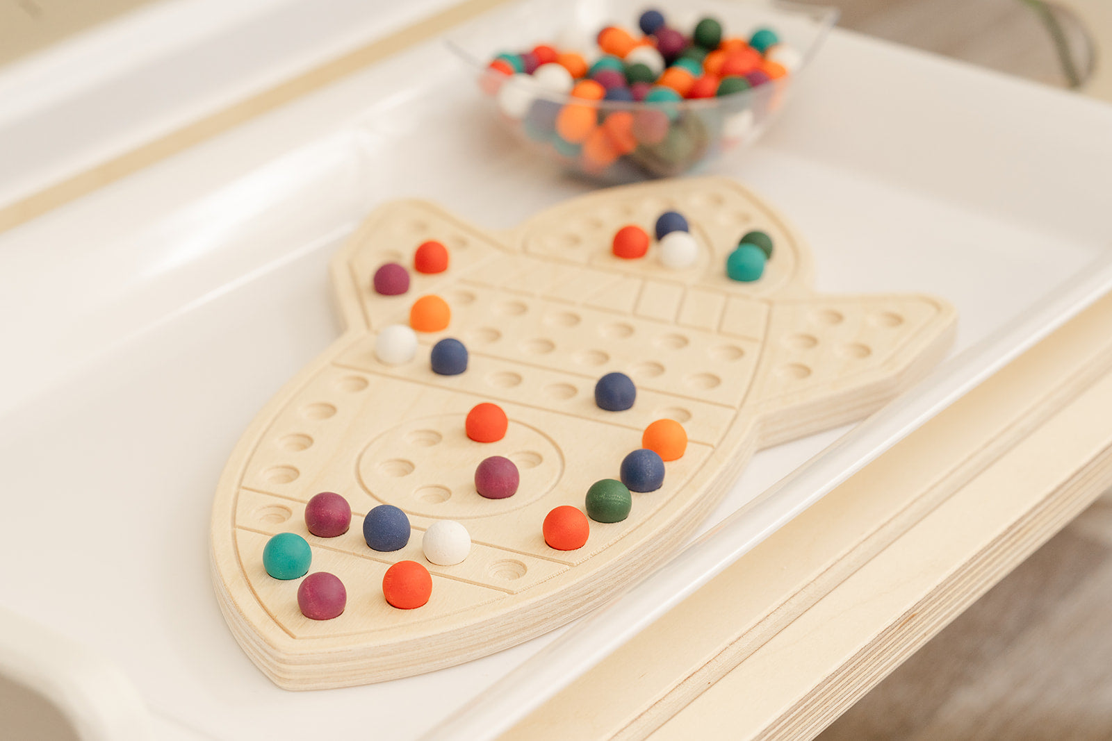 Wooden space activity board displayed in modern educational playroom with neutral decor demonstrating how STEM toys integrate into home environment. Screen-free sensory peg board for ages 3-6 providing quiet focused learning activity for preschoolers. USA-made wooden educational toy complementing minimalist playroom aesthetic while offering valuable hands-on STEM learning experience developing fine motor skills creativity and independent play habits through Montessori-inspired design.
