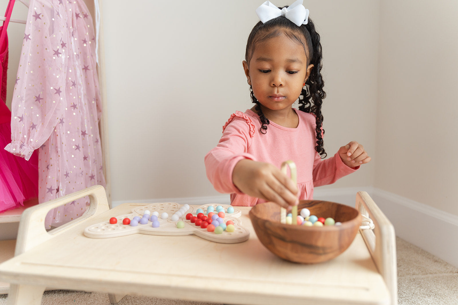 Young child using wooden tongs to pick up colorful balls and place them on butterfly activity board developing pincer grasp and hand strength. Montessori fine motor skills toy with included tongs promoting proper grip development and hand-eye coordination essential for writing readiness. Sensory peg board activity encouraging concentration patience and self-directed learning for preschool children ages 3-8 years through engaging tactile manipulation and educational play.