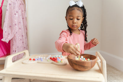 Young child using wooden tongs to pick up colorful balls and place them on butterfly activity board developing pincer grasp and hand strength. Montessori fine motor skills toy with included tongs promoting proper grip development and hand-eye coordination essential for writing readiness. Sensory peg board activity encouraging concentration patience and self-directed learning for preschool children ages 3-8 years through engaging tactile manipulation and educational play.