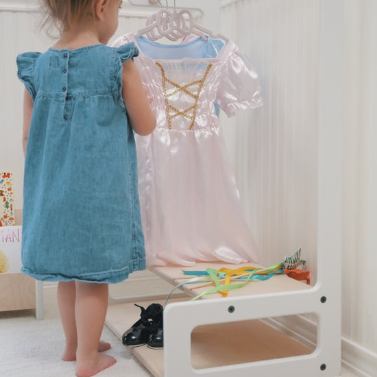 little girl playing with costumes on a kids clothing rack with shelves