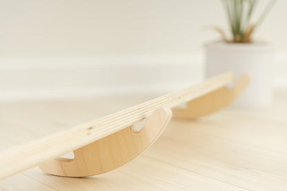 Side view of Preschool wobble beam showing curved base design for unique tilting balance challenge developing toddler gross motor skills. Wooden play furniture with smooth rocking motion stimulating vestibular system proprioception and body awareness for sensory processing development. USA-made birch plywood construction with non-toxic finish safe for young children exploring balance coordination and spatial orientation through open-ended active play experiences perfect for home or classroom environments.