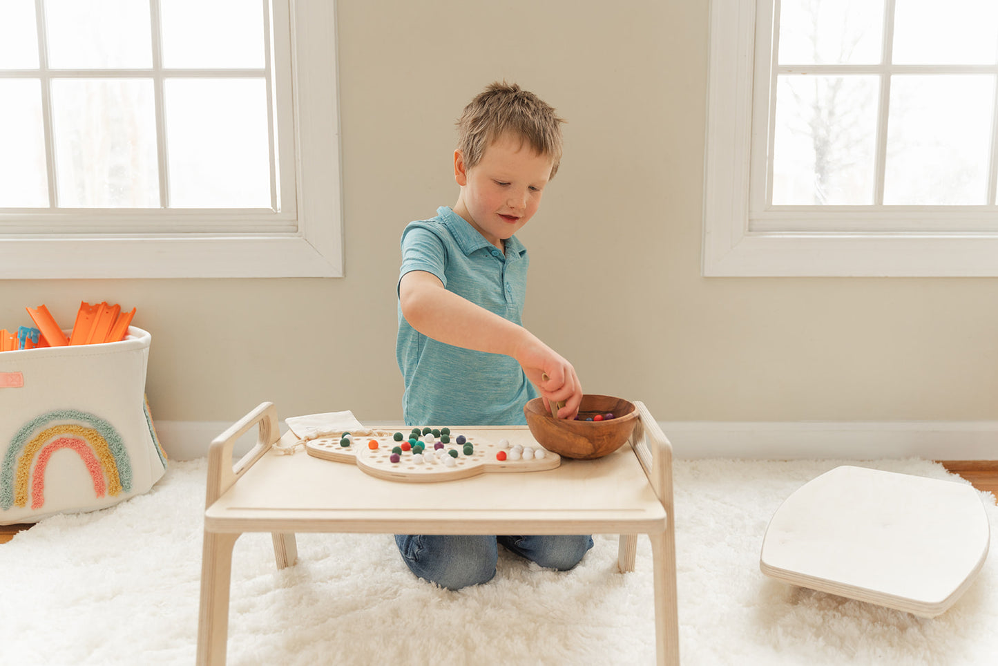 Toddler engaging in sensory play activities at wooden floor table with bins and manipulatives, child-sized activity table at perfect height for sitting or kneeling on floor demonstrating independent play and fine motor skill development, Montessori play tray encouraging exploration and hands-on learning for preschool-aged children in home or classroom setting