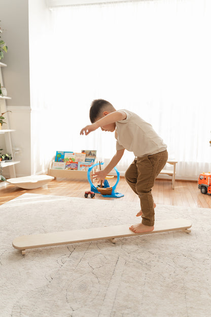 Wooden wobble beam incorporated into toddler obstacle course alongside balance beams creating comprehensive gross motor development activity. Montessori play furniture encouraging movement creativity and physical challenge for sensory seeking children ages 18 months to 6 years. Open-ended balance toy supporting vestibular stimulation coordination development and spatial awareness through dynamic tilting rocking action combined with other active play equipment for complete physical development experience in 