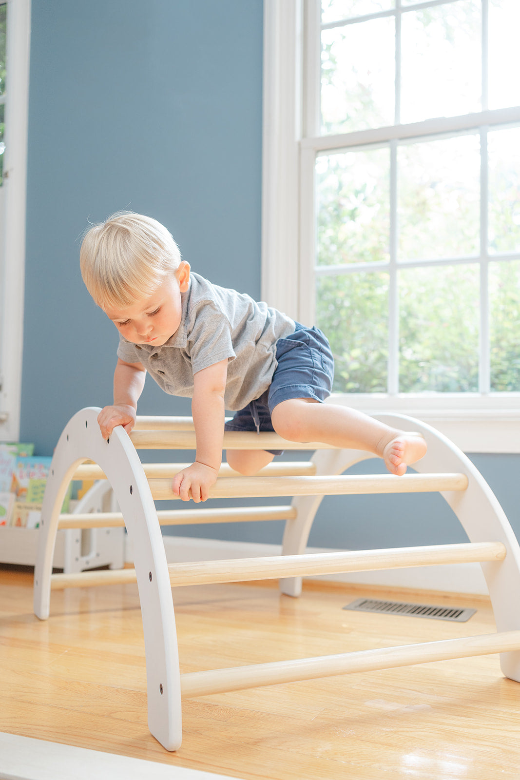 A toddler crawling over a climbing arch in a bedroom