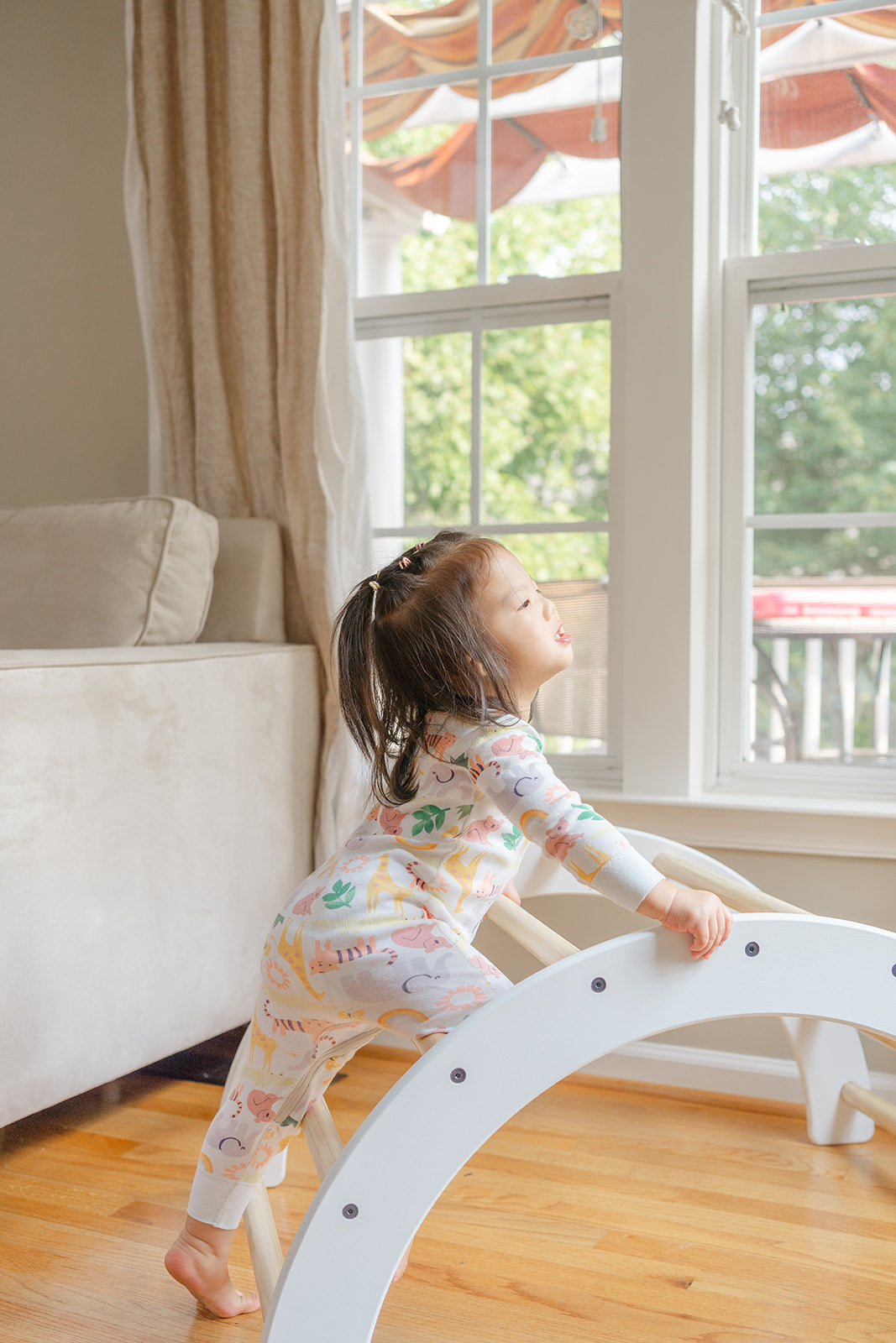 Child climbing on Montessori activity furniture showing how wooden arch serves as functional climbing equipment and active play structure, toddler using Pikler-inspired climber to develop gross motor skills through repeated climbing practice building muscle memory physical confidence and movement competence, indoor climbing toy designed as essential Montessori furniture piece for homes daycare centers and preschool classrooms supporting children's natural drive for movement and physical exploration ages 1-6