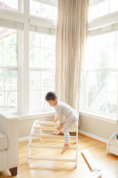 Toddler crawling over Montessori climbing arch demonstrating natural gross motor movement pattern and body coordination, child using wooden Pikler-inspired arch climber to practice climbing skills at own pace building confidence and open ended play, indoor climbing toy for toddlers supporting self-directed play and developmental milestones including upper body strength core stability hand-eye coordination and spatial problem-solving in safe low-to-ground design perfect for younger toddlers 12-24 months.