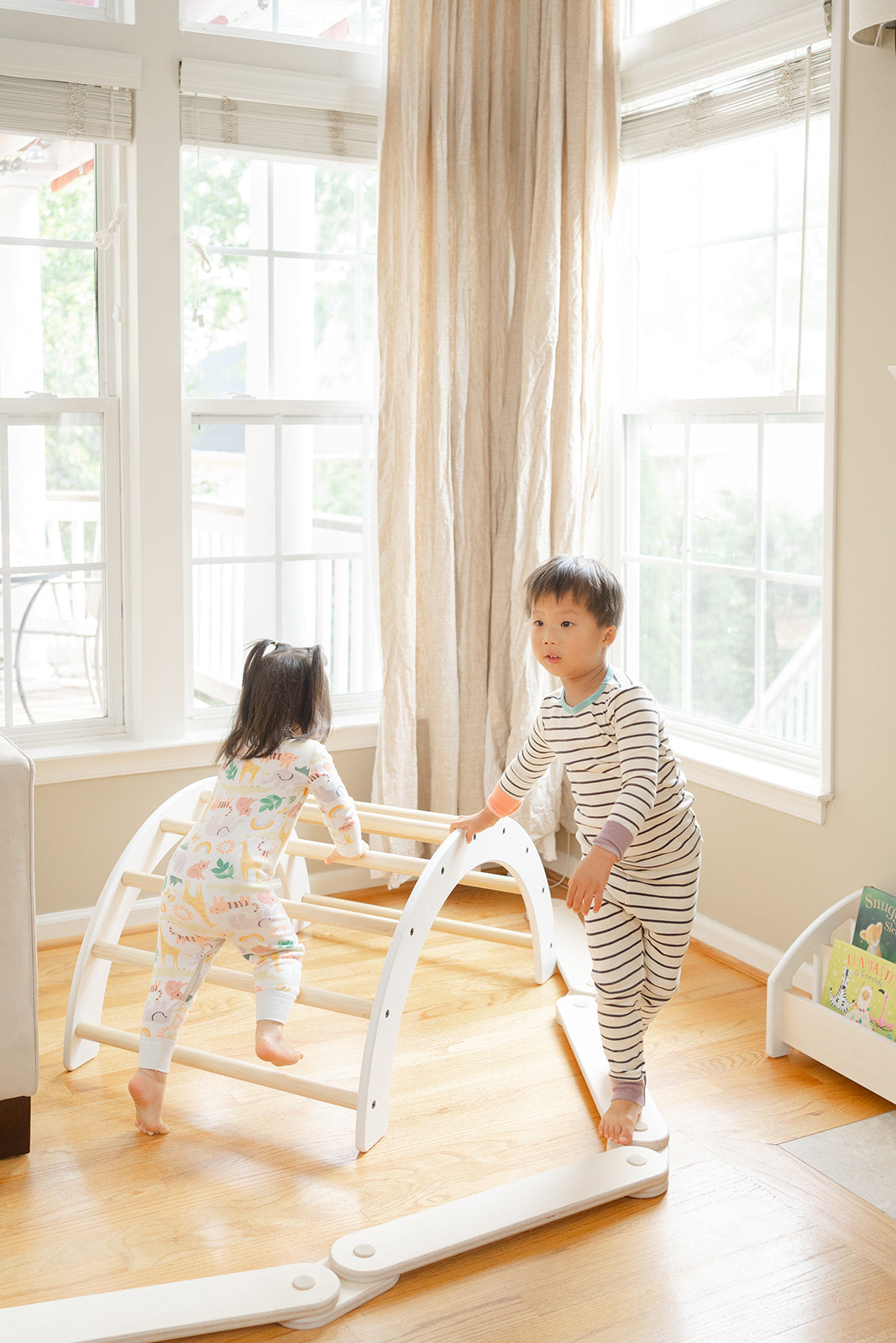 Multiple toddlers playing on Montessori wooden balance beam together developing social skills and taking turns on obstacle course, modular balance toy encouraging cooperative play and gross motor development for preschool-aged children in home or classroom