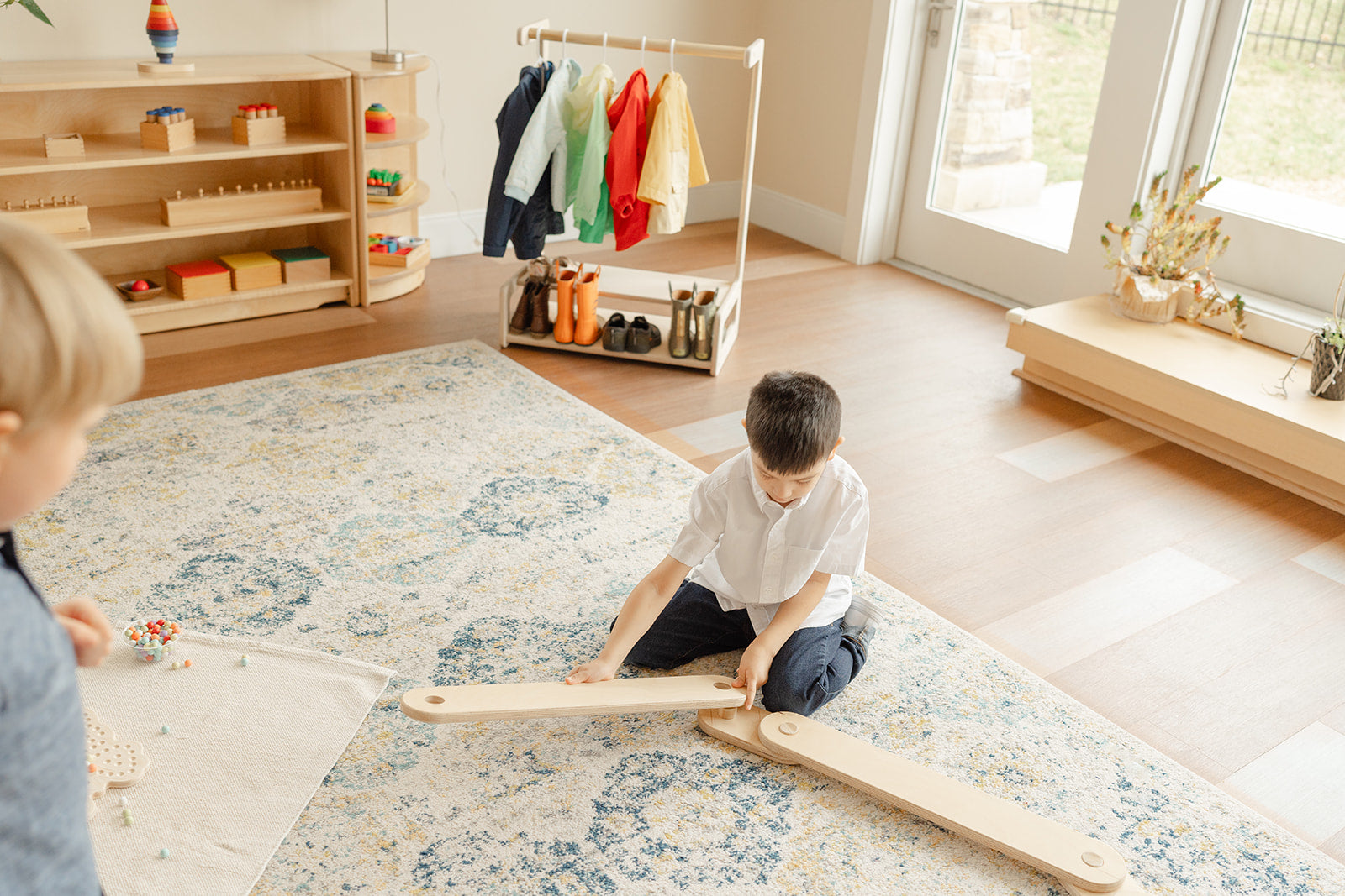 Primary Montessori aged boy putting together a long wooden balance beam on the ground to make an obstacle course 