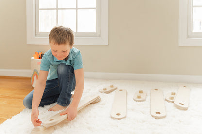 Preschooler independently connecting wooden balance beam pieces demonstrating STEM learning through hands-on problem-solving, child building custom obstacle course configuration developing fine and gross motor skills spatial reasoning and creative thinking through open-ended play