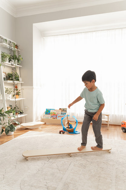 Wooden wobble beam displayed in modern Montessori playroom demonstrating how gross motor play furniture integrates into home environment. Balance board for sensory seeking toddlers providing vestibular stimulation proprioception development and coordination training through open-ended tilting rocking motion. USA-made play furniture complementing minimalist aesthetic while offering valuable physical development experience for children ages 18 months to 6 years building balance confidence and body awareness t