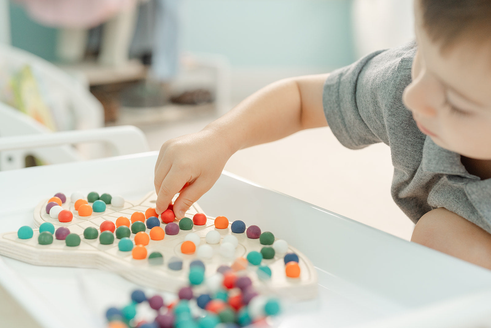 Beautiful and fun colorful balls placed on wooden rocketship played by young boy. The wooden rocketship puzzle helps with fine motor development and accompanied by bowl full of wooden balls