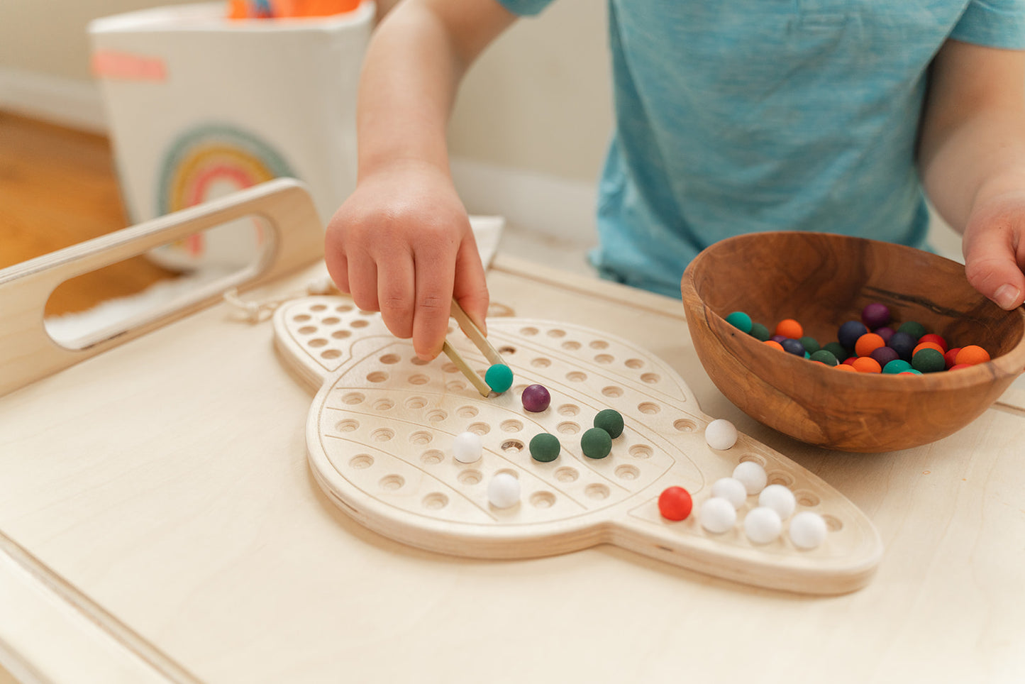 Close-up of vibrant multicolored wooden pegs and balls from Saturn activity board showing tactile sensory elements for hands-on learning. Colorful peg board toy with smooth wooden surfaces perfect for developing fine motor skills in elementary children ages 3-8. Open-ended educational STEM toy featuring rainbow wooden balls encouraging color recognition sorting pattern creation and creative problem-solving through Montessori-inspired space-themed play experiences with 98 pieces.