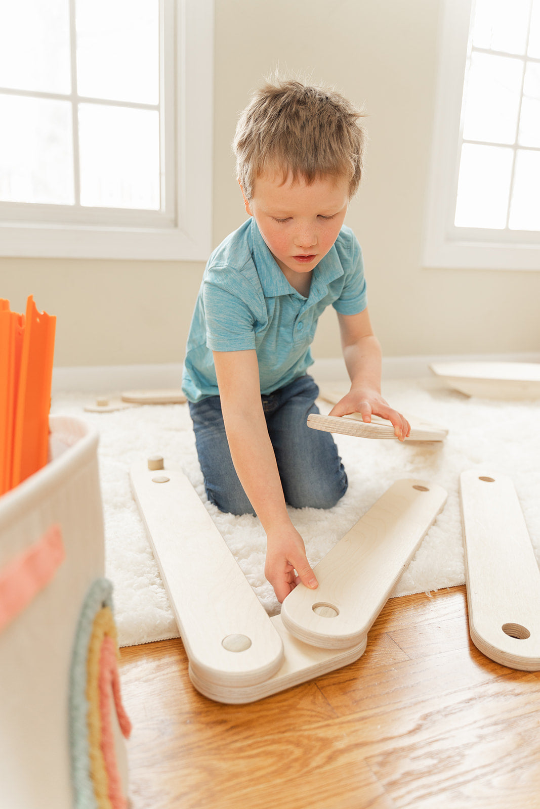 Wooden balance beam modular pieces stored compactly under living room couch demonstrating space-saving storage for small homes, beams and connectors easily disassemble for neat organization when not in use making perfect playroom toy for apartments and condos