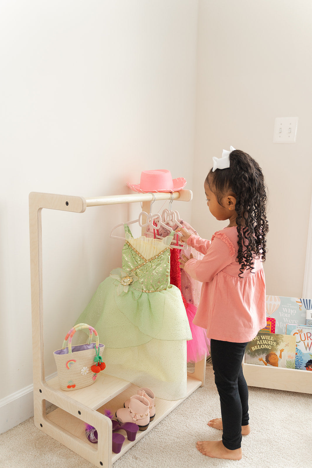 Young child independently reaching for clothes on toddler wardrobe rack at perfect child-height for autonomous dressing, Montessori kids clothing organizer empowering preschooler to select daily outfits without adult assistance, wooden children's garment rack with accessible hanging rod teaching organizational skills and morning routine independence, child-friendly clothing storage encouraging confident wardrobe choices and self-care habits.