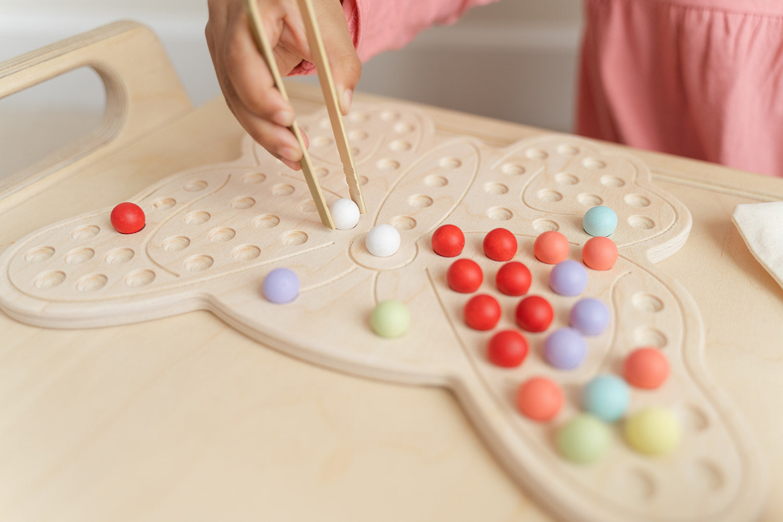 Child creating imaginative butterfly-inspired design with colorful wooden pegs on activity board showcasing unlimited open-ended play possibilities. Montessori sensory board encouraging self-expression artistic creativity and divergent thinking for ages 3-6. Educational peg board toy with no right or wrong way to play fostering confidence experimentation and creative problem-solving through tactile exploration and hands-on pattern creation in screen-free educational play environment.