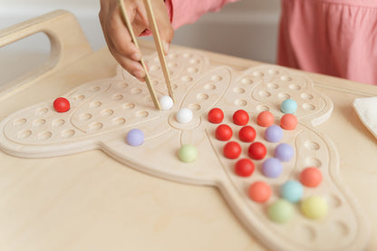 Child creating imaginative butterfly-inspired design with colorful wooden pegs on activity board showcasing unlimited open-ended play possibilities. Montessori sensory board encouraging self-expression artistic creativity and divergent thinking for ages 3-6. Educational peg board toy with no right or wrong way to play fostering confidence experimentation and creative problem-solving through tactile exploration and hands-on pattern creation in screen-free educational play environment.